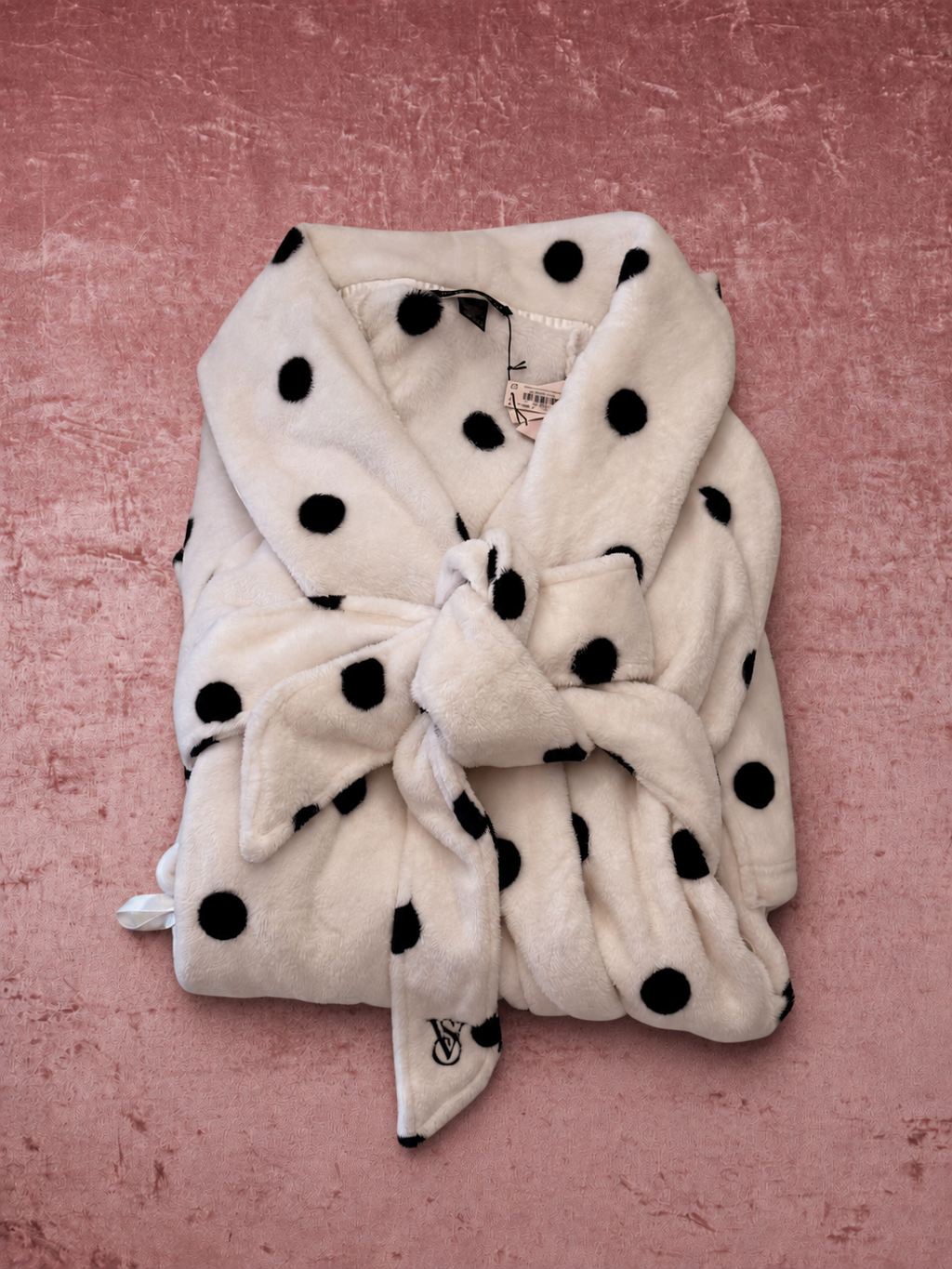 Bata V'S Blanca con Lunares Negros de Plush y Cinturón — vista plegada sobre fondo rosa texturado
