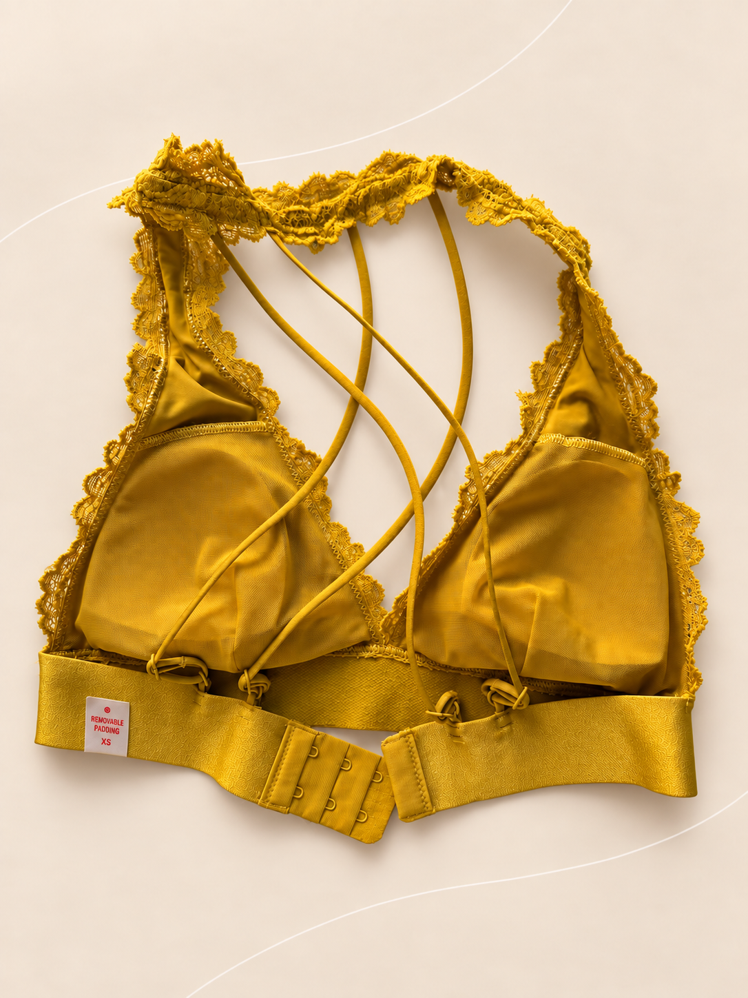 Bralette V'S de Encaje Mostaza con Tiras Cruzadas, vista dorsal sobre fondo crema de líneas suaves