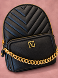 Mochila V'S negra con cadena dorada y sombra, vista 01