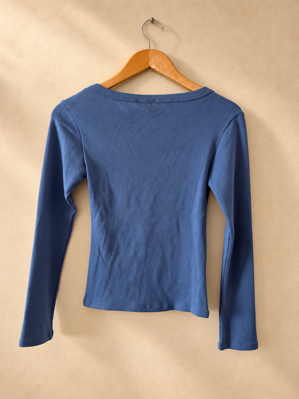 Dorso de Remera GUESS Azul de Manga Larga con Escote Amplio sobre fondo piedra cálida
