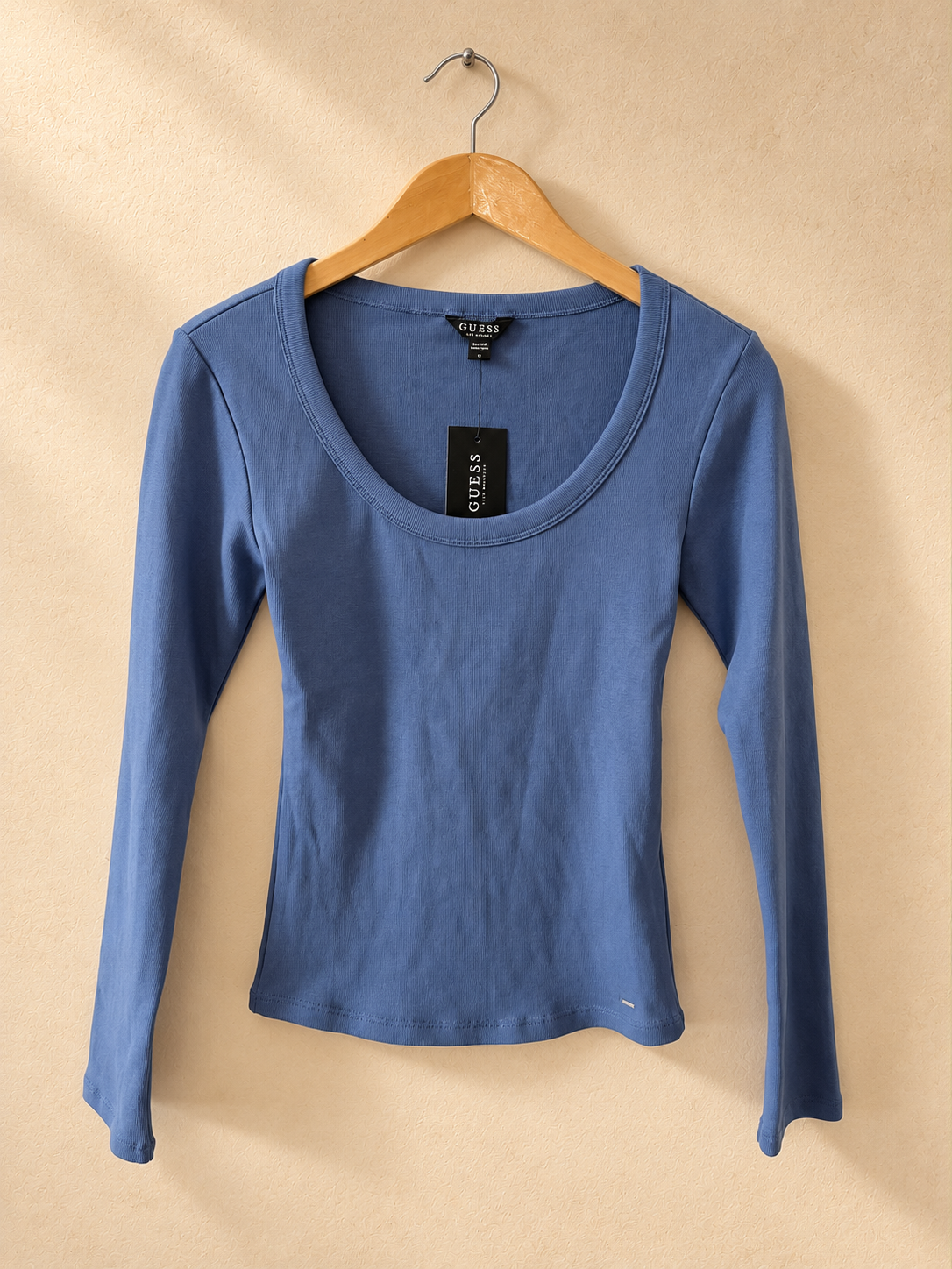 Frente de Remera GUESS Azul de Manga Larga con Escote Amplio sobre fondo piedra cálida