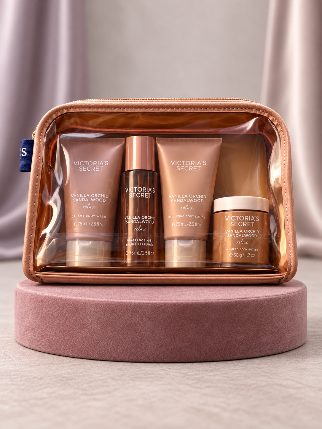 Set V'S Vanilla Orchid Sandalwood en neceser transparente, vista frontal sobre base rosa con cortinas malva